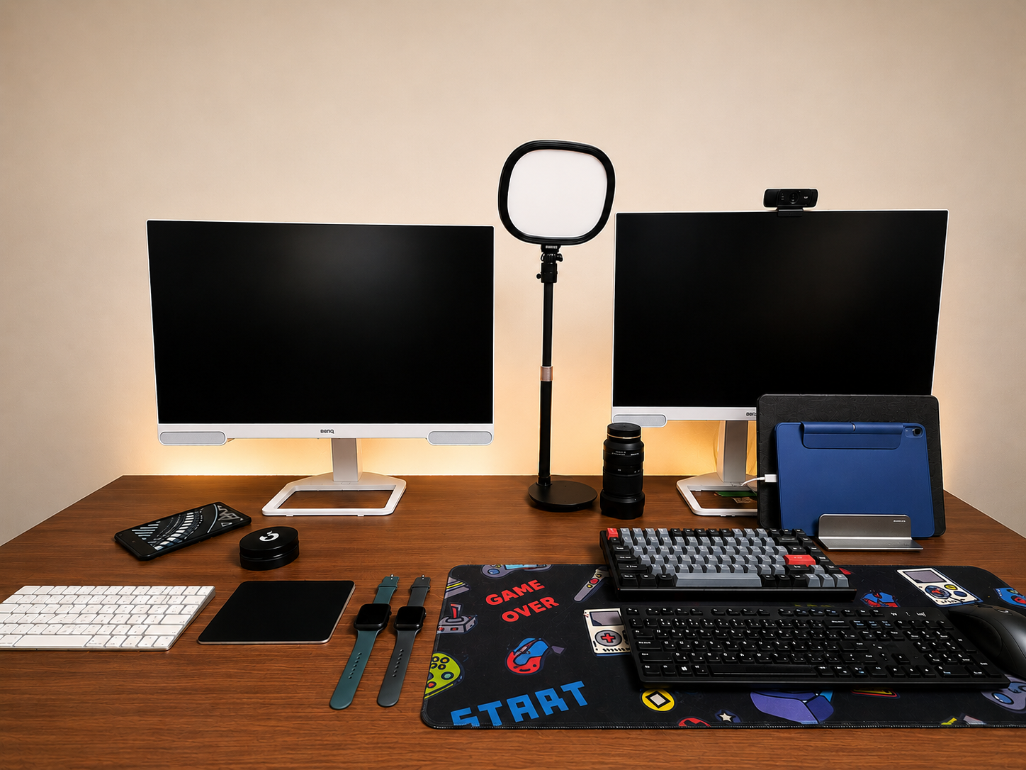 Two BenQ monitors on a walnut standing desk, with a Keychron K2, a Dell keyboard, an Apple Magic Keyboard and trackpad, a key light and a webcam